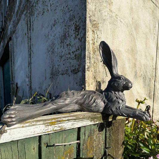 Grey hare resin statue lying down on a garden wooden fence