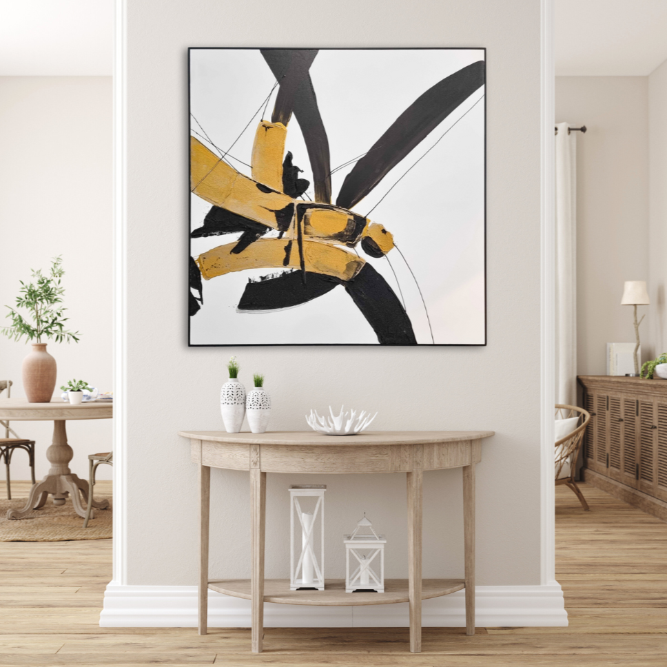 Kanji brush strokes in gold and black 
on a large painting. Cream wall with light coloured wood furniture behind a wall in the background. Infront of the painting is a semi circular console table in light wood with white vases and objects on it.