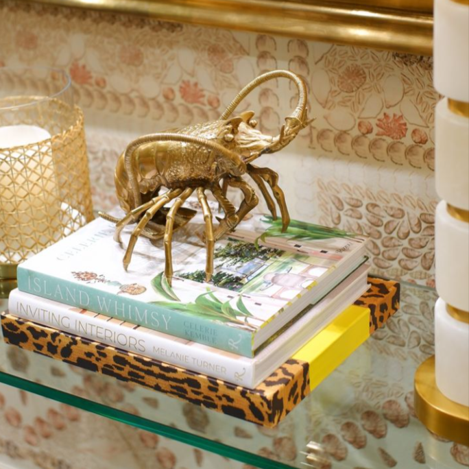 Brass Lobster from Eichholtz sitting on a stack of books on a glass shelf