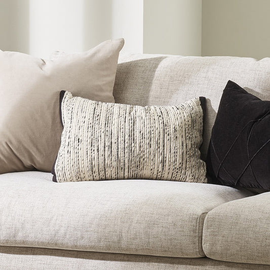 Odessa Cushion in cream and black sitting on a grey sofa with a grey and black cushion beside it