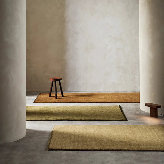 3 runner rugs in brown, green and beige on a stone floor with stone walls and two stone pillars with a wooden stool sitting on the brown rug
