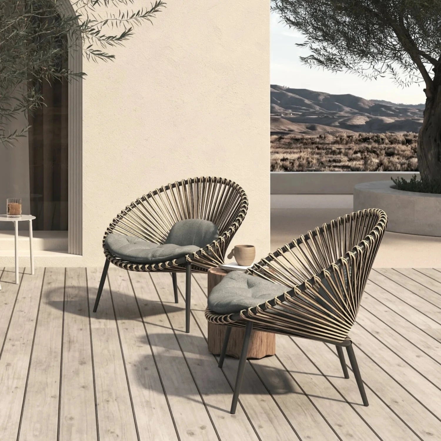 two wicker lounge chairs on a wooden deck with spanish countryside in the back ground and a plastered house of the wall in the background
