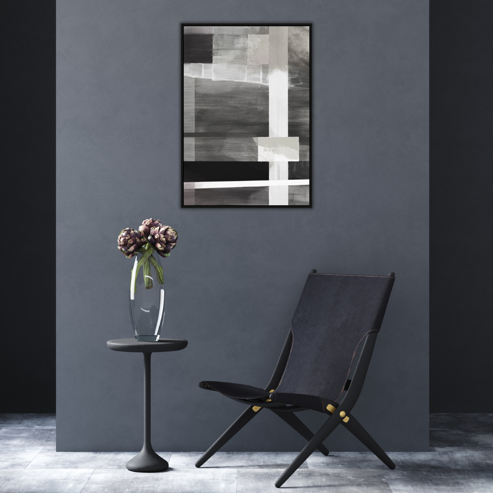 Black and white abstract art work hanging on a grey wall above a black armless chair and a small black side table with a glass vase full of peach flowers