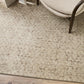 Cadence rug, cream back ground with a mottled brown hand blocked pattern. Show with a brown wooden chair with a boucle seating in cream.