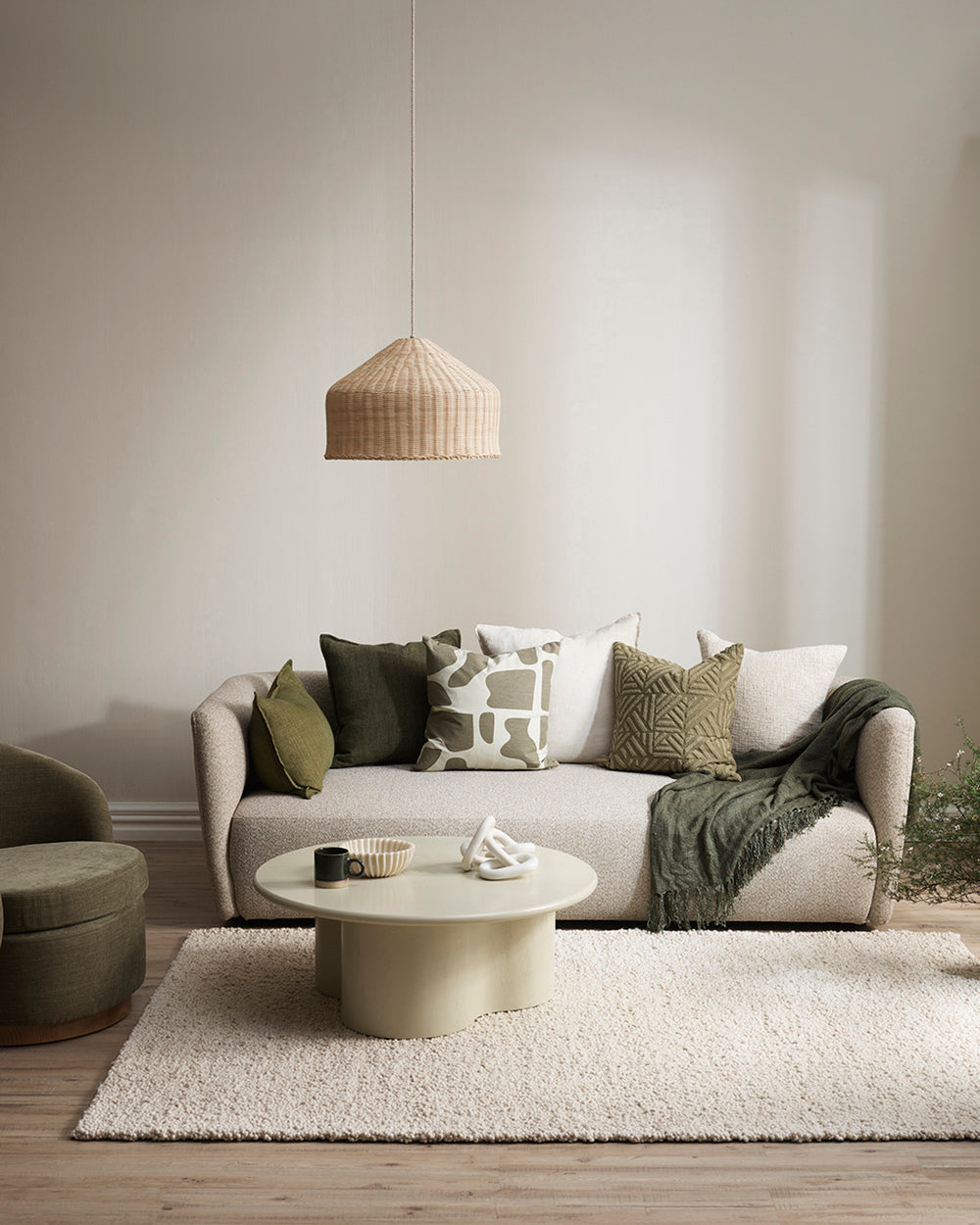 Harper cushion with cream back ground and abstract olive sploges from the Baya Collection in lifestyle shot with other cushions, cream sofa and rug, rattan lamp shade