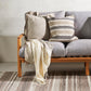 two cushions in neutral colours one striped and one plain on a grey sofa with wooden handles. 