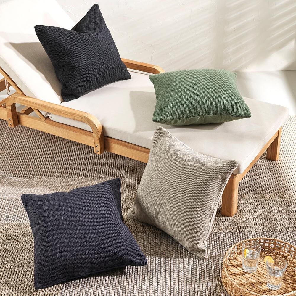 Southwold cushions in black, navy, olive and ecru scattered on the floor and on a wooden and linen outdoor lounger seat