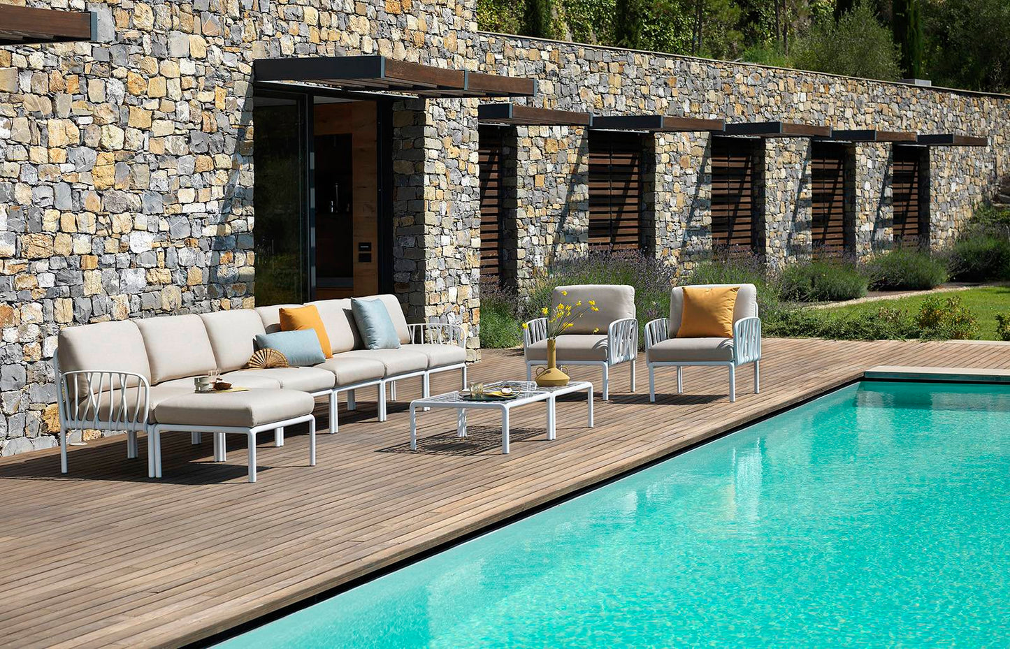 Komodo Outdoor Chair, white frame, grey cushion around the pool by a stonen wall